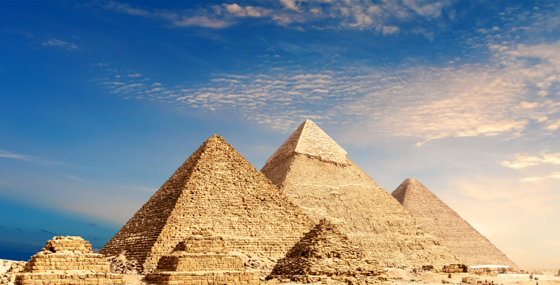 The Great Pyramids of Giza under a clear blue sky, with the pyramids' ancient stones illuminated by sunlight.