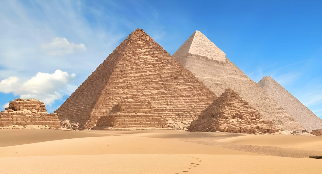 Three large pyramids and smaller ones stand in a desert landscape under a blue sky.