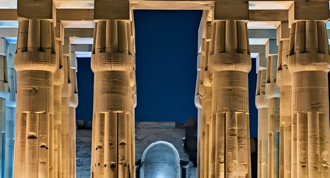 Majestic night view of ancient stone columns and an archway, illuminated against a deep blue sky.