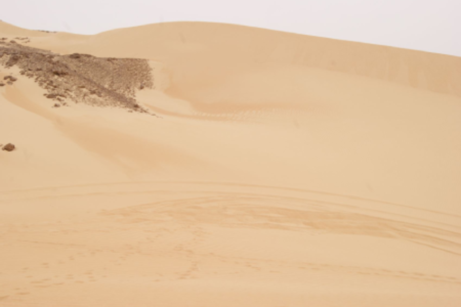 A desert landscape with sand dunes and faint tire tracks.