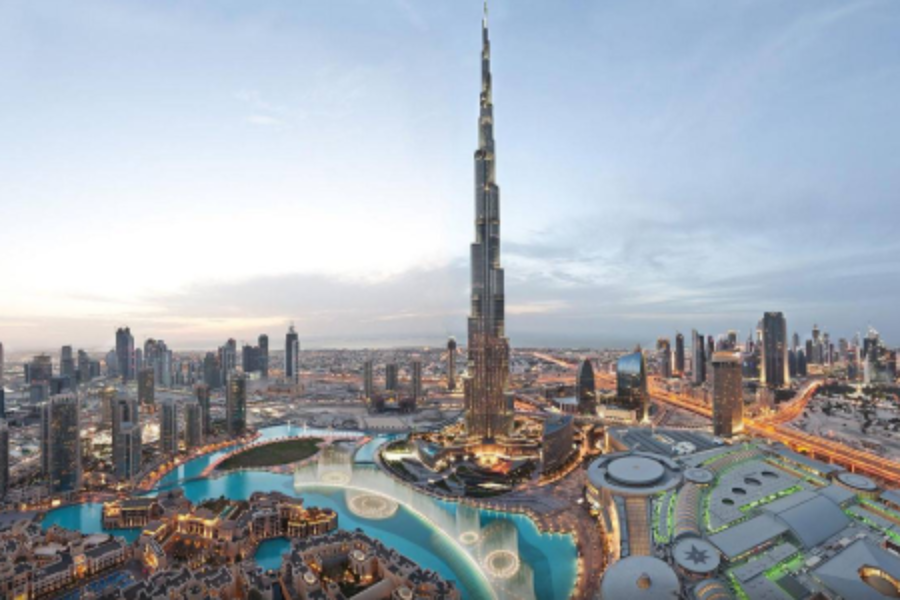 Aerial view of a cityscape featuring the tall Burj Khalifa surrounded by illuminated buildings and water features at dusk.