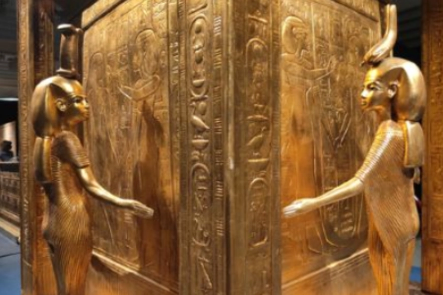 Golden Egyptian sarcophagus with hieroglyphs and two carved figures on each side, standing opposite each other.